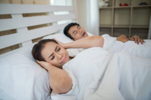 Portrait of woman blocking ears with man sleeping snoring on bed