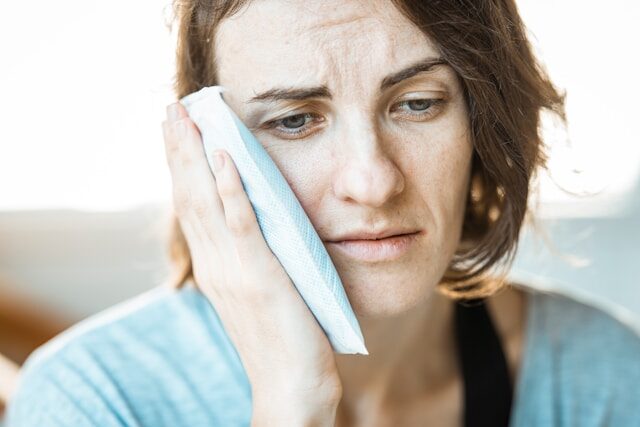 woman in blue holding side of face