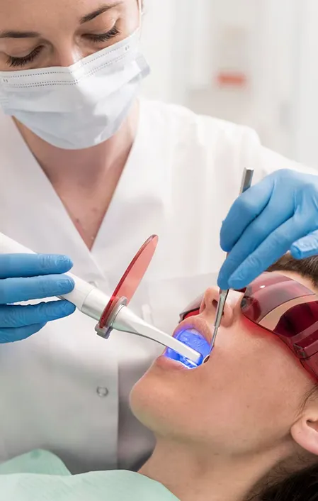 dentist using dental UV curing light to set new dental tooth filling in a patient