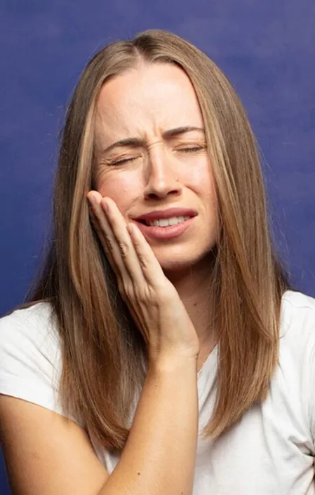 woman white shirt holding side of face with tooth pain and decay